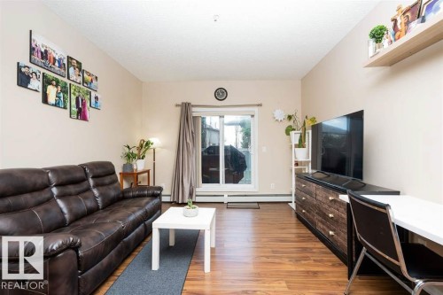 Living area featuring wood-finish flooring, light-toned walls, and a sliding glass door - #117 226 Macewan Sw, Edmonton, AB - Indoor Photo Showing Living Room