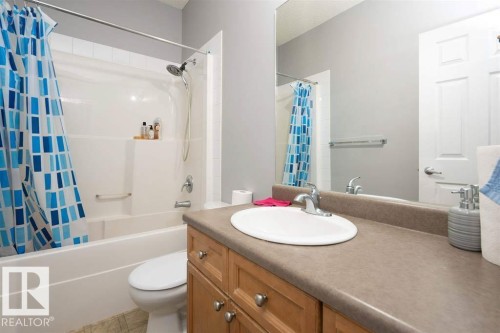 Bathroom featuring a full vanity with an integrated sink, wood-finish cabinetry, and a spacious countertop - #117 226 Macewan Sw, Edmonton, AB - Indoor Photo Showing Bathroom
