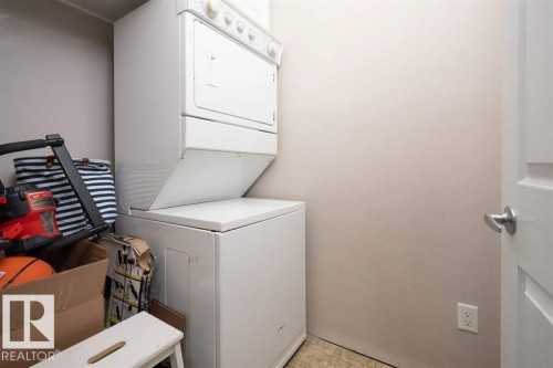 Laundry area featuring a stacked washer and dryer unit, neutral wall paint, and a paneled door with a brushed nickel handle - #117 226 Macewan Sw, Edmonton, AB - Indoor Photo Showing Laundry Room
