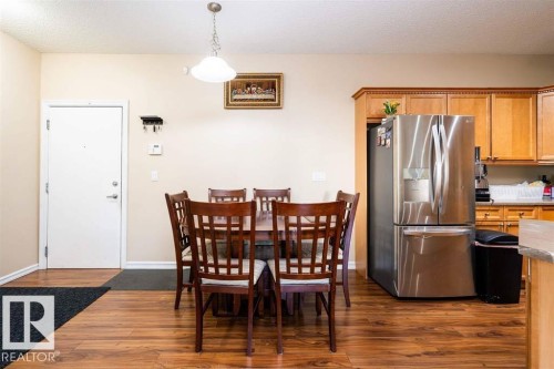 Open-concept dining area featuring wood-finish flooring, a contemporary pendant light fixture, and a stainless steel refrigerator - #117 226 Macewan Sw, Edmonton, AB - Indoor Photo Showing Other Room