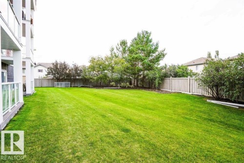 Expansive green lawn with mature trees and a privacy fence - #117 226 Macewan Sw, Edmonton, AB - Outdoor With Backyard