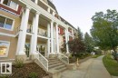 Multi-story building featuring classical columns, glass-paneled balconies, a concrete sidewalk, and mature landscaping with evergreen trees - #117 226 Macewan Sw, Edmonton, AB  - Outdoor 