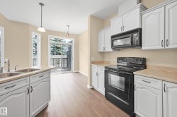 Kitchen featuring wood-finish flooring, white cabinetry with dark hardware, a double basin stainless steel sink, and a black appliance suite - 