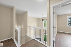 Open landing featuring wood-finish flooring, white trim, and a staircase with white newel posts and dark metal balusters - 