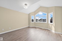 Spacious room featuring vaulted ceilings, a large bay window with multiple panes, two additional vertical windows, wood-finish flooring, and a flush-mount ceiling light fixture - 