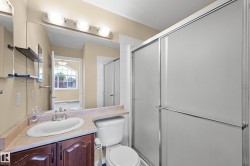 Bathroom featuring a single-basin vanity with a wood-finish cabinet, a light-toned countertop, a large wall-mounted mirror, and a shower with frosted sliding doors - 