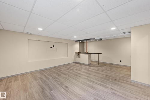 Finished basement space featuring wood-finish flooring, a drop ceiling with recessed lighting, an integrated media niche, and a built-in wet bar with a dark countertop - 11544 11 Avenue, Edmonton, AB 