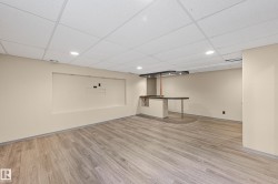 Finished basement space featuring wood-finish flooring, a drop ceiling with recessed lighting, an integrated media niche, and a built-in wet bar with a dark countertop - 