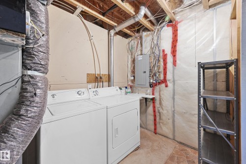 Utility area featuring a washer and dryer, exposed ceiling joists, an electrical service panel, and a metal storage shelf - 11544 11 Avenue, Edmonton, AB 