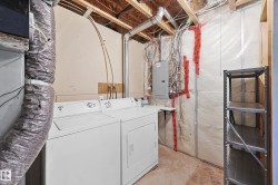 Utility area featuring a washer and dryer, exposed ceiling joists, an electrical service panel, and a metal storage shelf - 