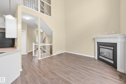 Living area featuring wood-finish flooring, a corner fireplace with a white mantel, and high ceilings - 11544 11 Avenue, Edmonton, AB 