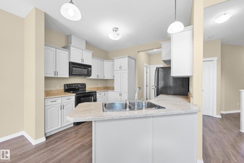 Kitchen featuring wood-finish flooring, white cabinetry, integrated black appliances, and pendant lighting - 11544 11 Avenue, Edmonton, AB 