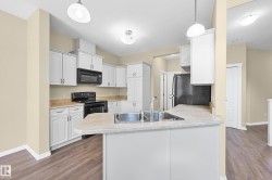 Kitchen featuring wood-finish flooring, white cabinetry, integrated black appliances, and pendant lighting - 