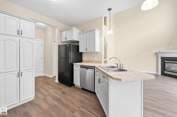 Kitchen featuring white cabinetry, a black refrigerator, stainless steel dishwasher, and wood-finish flooring - 