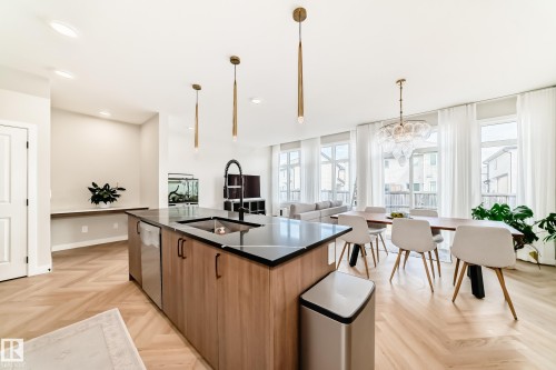 Open-concept kitchen and dining area featuring herringbone wood-finish flooring, a kitchen island with a black countertop and integrated sink, stainless steel appliances, and a dining area with multiple windows - 4231 206 Street, Edmonton, AB 