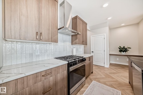Gourmet kitchen featuring wood-finish cabinetry, stainless steel range, and a coordinating stainless steel range hood - 4231 206 Street, Edmonton, AB 