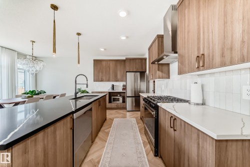 Contemporary kitchen featuring wood-finish cabinetry, black and white countertops, a stainless steel gas range, and a full-size stainless steel refrigerator - 4231 206 Street, Edmonton, AB 