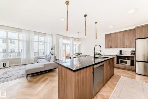 Open-concept living space featuring herringbone wood-finish flooring, a kitchen island with a dark countertop and undermount sink, stainless steel appliances, and multiple large windows - 4231 206 Street, Edmonton, AB 