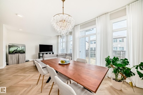 Open-concept living space featuring herringbone wood-finish flooring, a modern dining area with a rectangular wood-top table, and a contemporary chandelier - 4231 206 Street, Edmonton, AB 