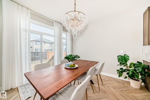 Dining area featuring a contemporary chandelier, large windows with full-length sheer curtains, herringbone wood-finish flooring, and light neutral wall tones - 4231 206 Street, Edmonton, AB 