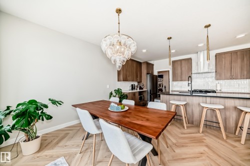 Herringbone wood-finish flooring complements the dining area, featuring a decorative chandelier and a solid wood dining table - 4231 206 Street, Edmonton, AB 