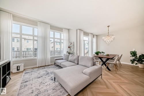 Open-concept living area featuring large pane windows, herringbone wood-finish flooring, and a contemporary chandelier - 4231 206 Street, Edmonton, AB 
