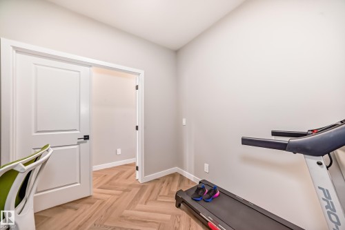 Interior room featuring light-toned walls, a white two-panel door with black hardware, and wood-finish flooring laid in a herringbone pattern - 4231 206 Street, Edmonton, AB 