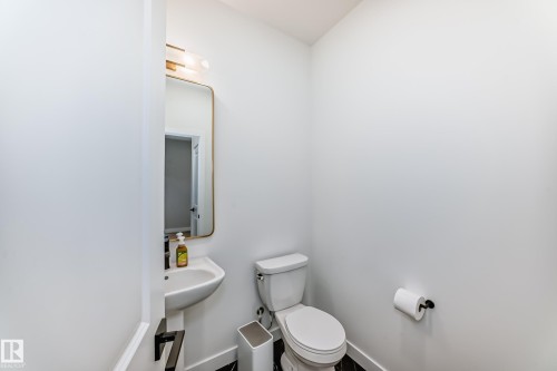 Powder room featuring a pedestal sink with a matte black faucet, wall-mounted mirror with an overhead light fixture, and a toilet - 4231 206 Street, Edmonton, AB 