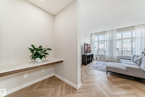 Open-concept living space featuring light wood-finish herringbone flooring, large windows with vertical blinds, and a built-in wall-mounted console with a light-toned countertop - 4231 206 Street, Edmonton, AB 