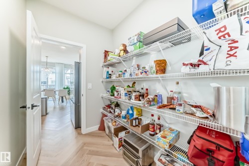 Expansive pantry featuring multiple wire shelving units, light wood-finish flooring with a herringbone pattern, and a doorway opening to an additional interior space - 4231 206 Street, Edmonton, AB 