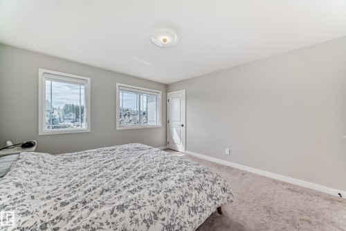 Carpeted room with two large windows, a solid white door with black hardware, white baseboards, and a flush-mount ceiling light fixture - 4231 206 Street, Edmonton, AB 