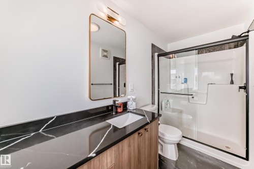 Bathroom featuring a black countertop with white veining, an undermount sink, and wood-finish cabinetry - 4231 206 Street, Edmonton, AB 