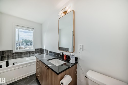 Modern bathroom featuring a wood-finish vanity with a black countertop and rectangular undermount sink - 4231 206 Street, Edmonton, AB 
