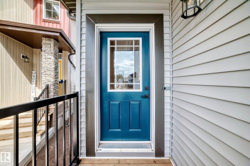 Vibrant blue entry door with decorative glass panels, framed by dark trim, set against light horizontal siding - 4231 206 Street, Edmonton, AB 