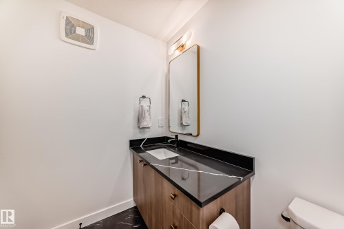 Modern bathroom vanity featuring a wood-finish cabinet with black hardware, a dark countertop with white veining, an undermount sink, and a black faucet - 4231 206 Street, Edmonton, AB 