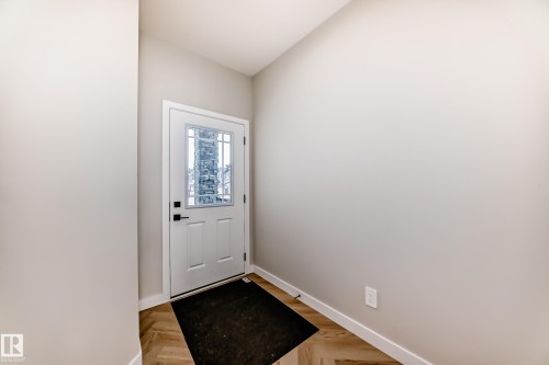 White front entry door with decorative glass inserts and matte black hardware, framed by light-toned walls - 4231 206 Street, Edmonton, AB 
