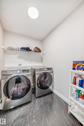Laundry area featuring dark-toned stone-finish flooring, a wall-mounted wire shelf, a ceiling light fixture, and a neutral wall color - 4231 206 Street, Edmonton, AB 