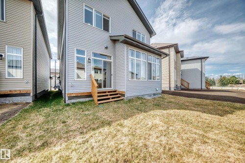 Rear elevation featuring light gray siding, a sunroom with multiple windows, a sliding glass door, a wooden staircase, and an expansive lawn area - 4231 206 Street, Edmonton, AB 