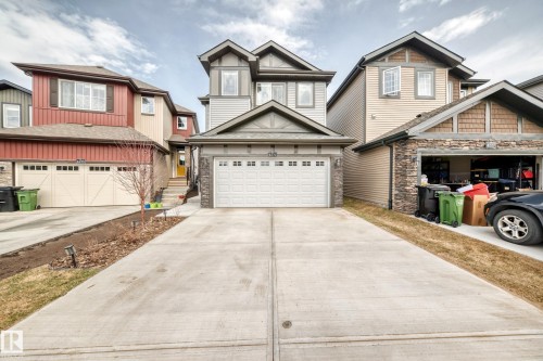 Contemporary two-story residence featuring a prominent attached garage with a white sectional door, stone veneer detailing, and a concrete driveway - 4231 206 Street, Edmonton, AB 