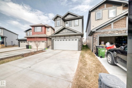 Two-story home with a light gray siding exterior, stone veneer accents, and a white paneled garage door - 4231 206 Street, Edmonton, AB 