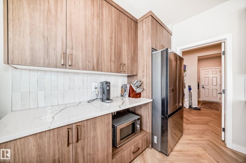 Integrated stainless steel refrigerator, white quartz countertops with subtle veining, and wood-finish cabinetry - 4231 206 Street, Edmonton, AB 