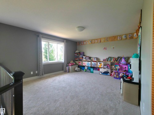 Spacious carpeted room featuring a large window with white trim, dark grey walls, and a contemporary ceiling light fixture - 1 Hemlock Close, Fort Saskatchewan, AB 
