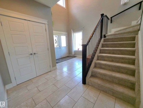 Foyer featuring plank-style tile flooring, a carpeted staircase with a dark wood and iron railing, a panel-style entry door with decorative glass, and a pair of panel-style closet doors - 1 Hemlock Close, Fort Saskatchewan, AB 