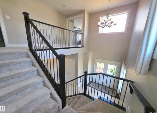 Two-story foyer featuring a grand staircase with dark wood banisters and metal spindles, carpeted stairs, and an elegant chandelier - 1 Hemlock Close, Fort Saskatchewan, AB 