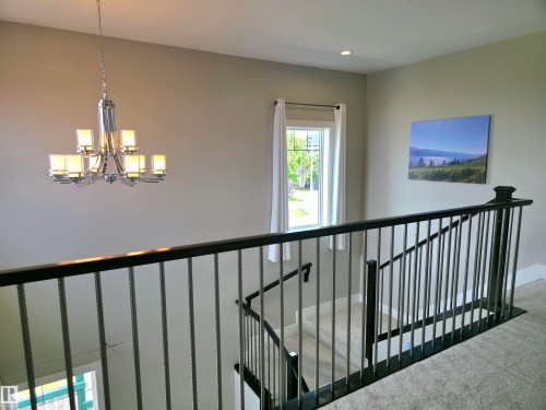 Carpeted hallway featuring a decorative chandelier, recessed lighting, and a window with white drapes - 1 Hemlock Close, Fort Saskatchewan, AB 