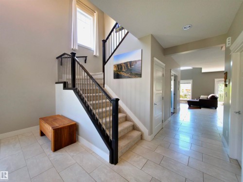Spacious foyer featuring light-toned tile flooring, a carpeted staircase with dark wood newel posts and metal balusters, and a large window providing natural light - 1 Hemlock Close, Fort Saskatchewan, AB 