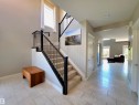 Spacious foyer featuring light-toned tile flooring, a carpeted staircase with dark wood newel posts and metal balusters, and a large window providing natural light - 1 Hemlock Close, Fort Saskatchewan, AB 