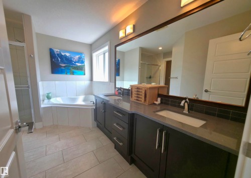 Bathroom featuring a double vanity with dark cabinetry, integrated sinks, and a single large mirror - 1 Hemlock Close, Fort Saskatchewan, AB 