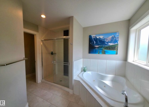Corner soaking tub with white tile surround, adjacent to a glass-enclosed shower featuring light and dark tile accents - 1 Hemlock Close, Fort Saskatchewan, AB 