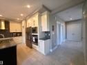 Gourmet kitchen featuring a large island with an undermount sink, stainless steel appliances, white cabinetry with contemporary hardware, and light-toned tile flooring - 1 Hemlock Close, Fort Saskatchewan, AB 